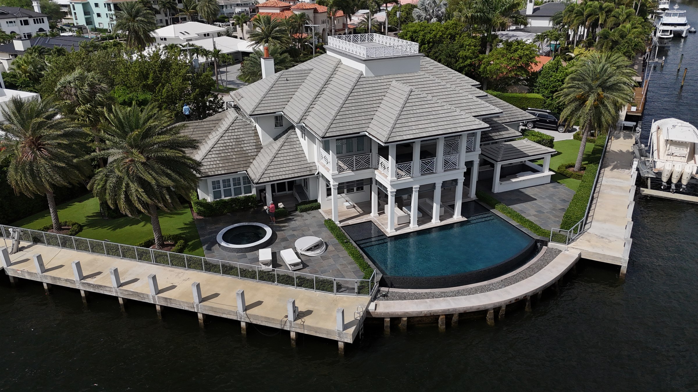 Aerial view of a waterfront home with a tile roof, pool, and tropical landscaping