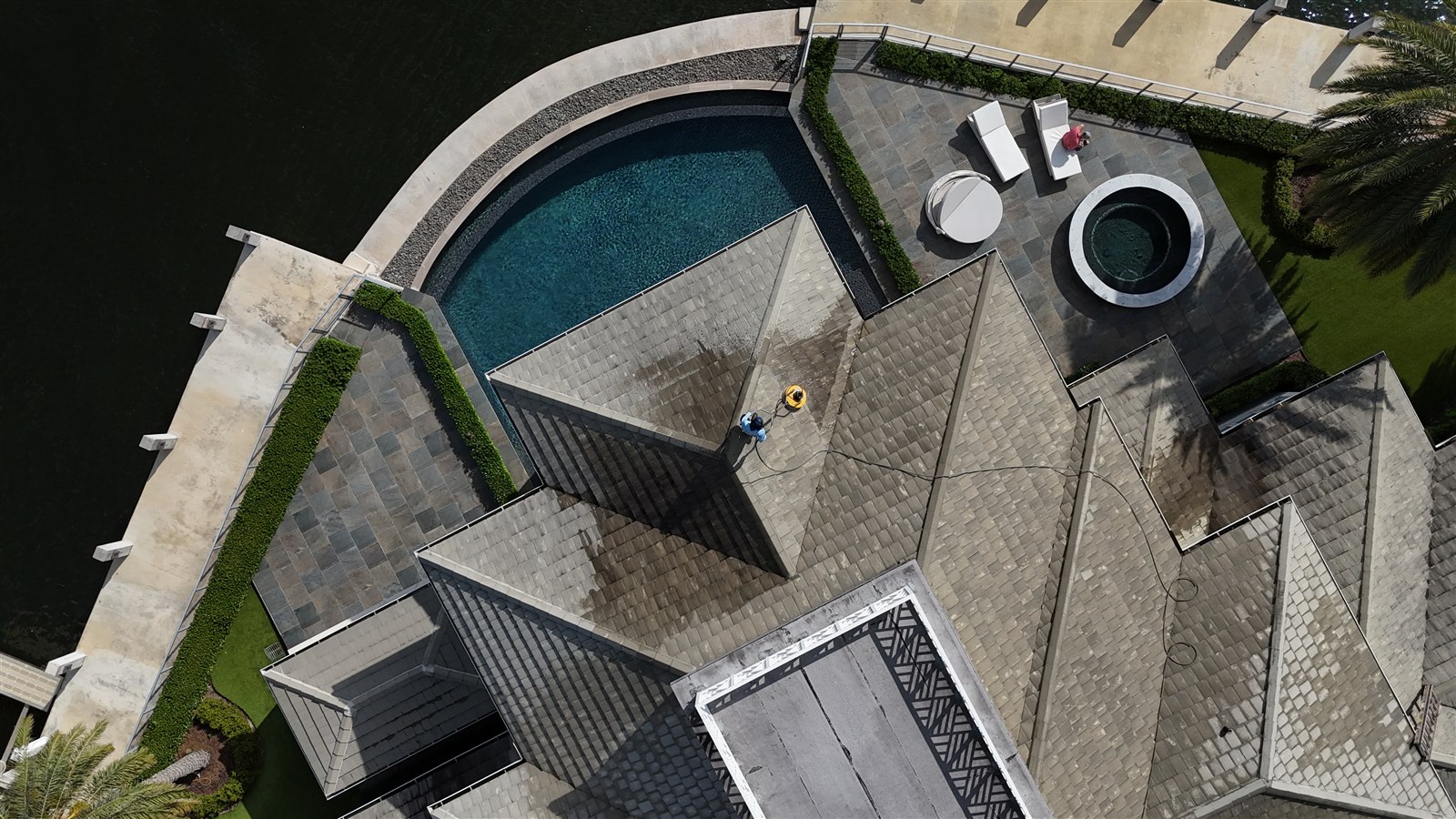 Aerial view of a team member cleaning the tile roof of a waterfront home